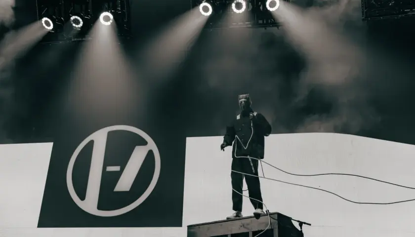 Tyler Joseph z Twenty One Pilots na scenie w Łodzi, w charakterystycznym stroju, na tle logo zespołu.