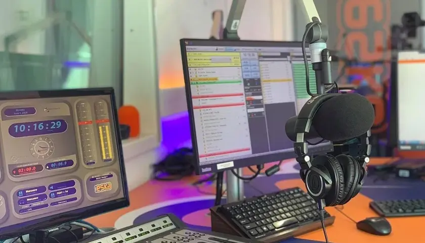 W studiu radiowym, gdzie słychać muzykę z **radio eska2 online**, wiszą słuchawki. Na monitorach widać zegar i program radiowy.