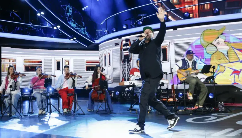Wokalista na scenie podczas festiwalu Opole, z orkiestrą smyczkową i gitarzystą w tle.