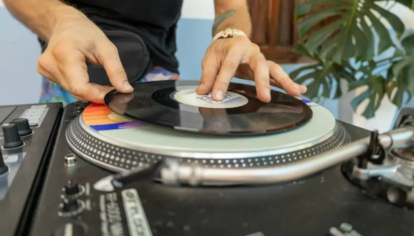 DJ kładzie winylową płytę na gramofonie. Kolorowy **cover** pod nią dodaje klimatu.