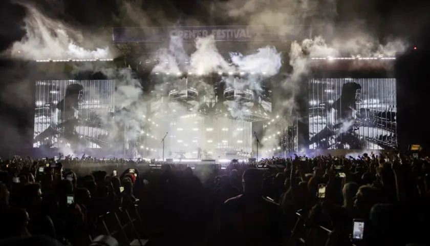 Koncert Linkin Park Polska na Open'er Festival. Tłum ludzi z telefonami, dym i światła na scenie.