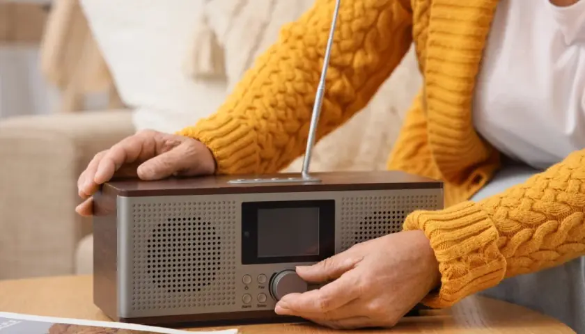 Dłoń kręci pokrętłem radia, by posłuchać RMF FM w pracy.