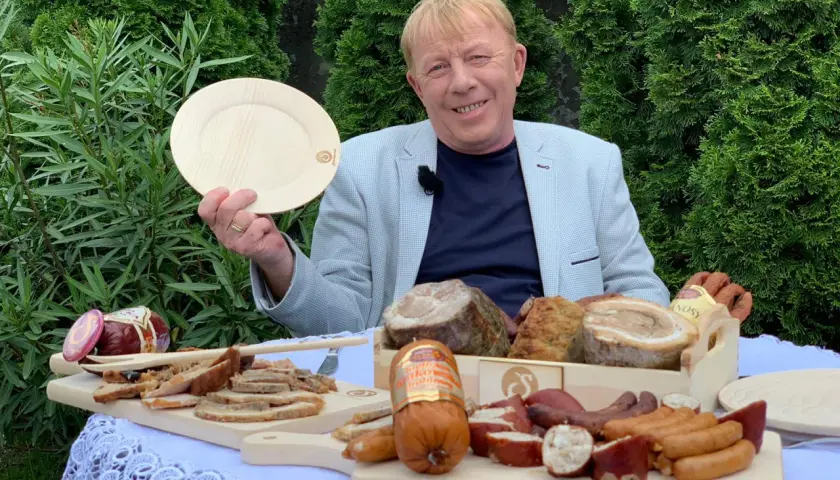 Mirek Szołtysek prezentuje bogactwo wędlin i mięs na drewnianych deskach, trzymając w dłoni pusty talerz.