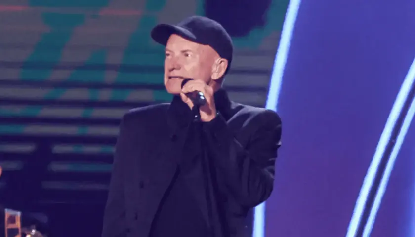 Sting w czapce i czarnym stroju śpiewa do mikrofonu. Ciekawe, ile Sting bierze za koncert, gdy występuje na tak dużej scenie.