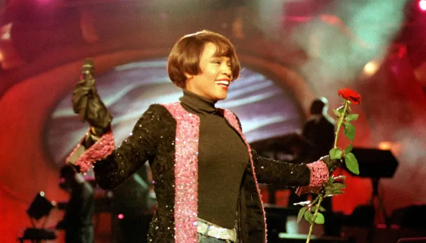Whitney Houston w Polsce, na scenie z mikrofonem i czerwoną różą, w błyszczącej marynarce.