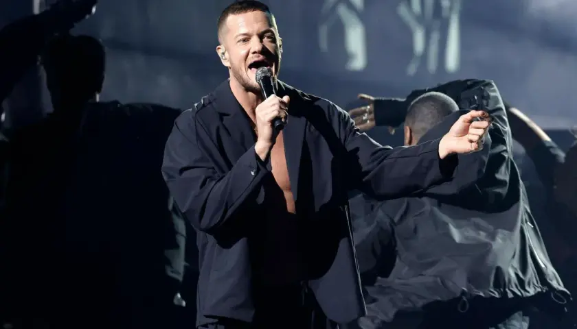 Imagine Dragons koncert Polska: wokalista Dan Reynolds śpiewa na scenie, otoczony tancerzami w mrocznej atmosferze.