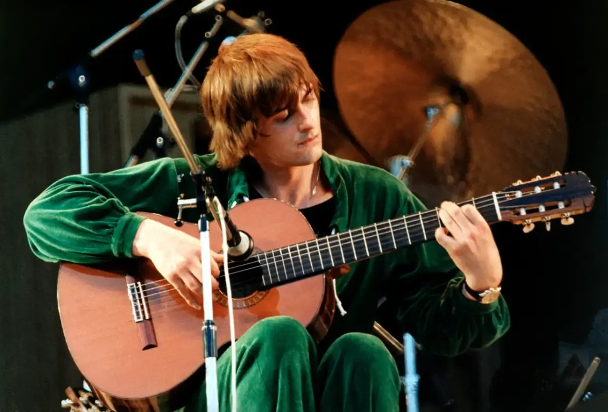 Mężczyzna w zielonym dresie gra na gitarze, a jego twarz skrywa się w **moonlight shadow**.