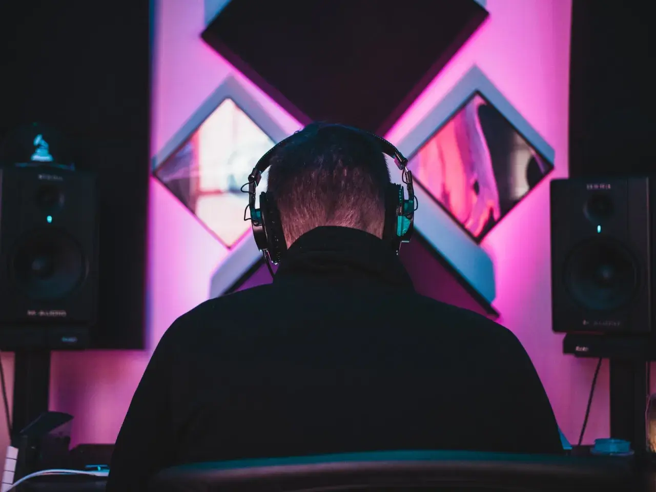 DJ w słuchawkach tworzy taneczne hity wszechczasów w studiu z neonowym oświetleniem.