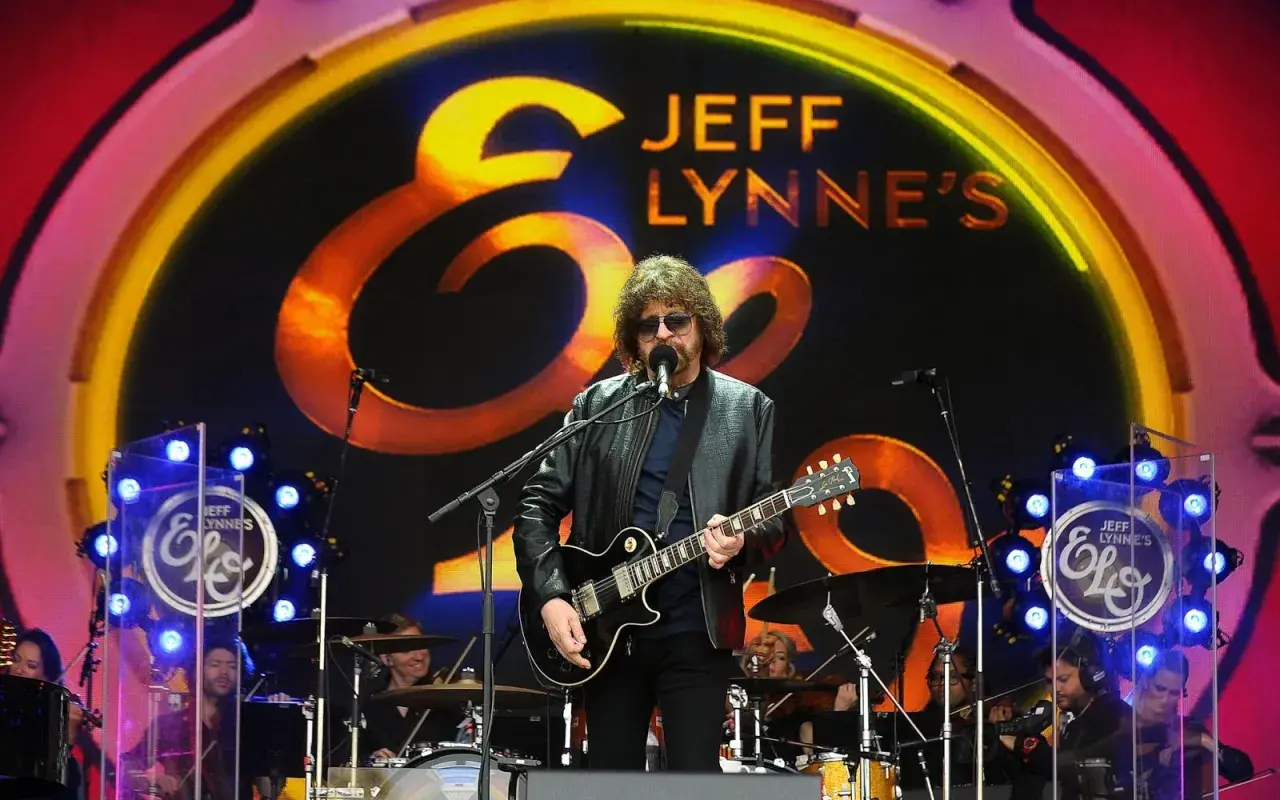 Jeff Lynne z Electric Light Orchestra na scenie, wykonuje swoje kultowe utwory. W tle logo zespołu.