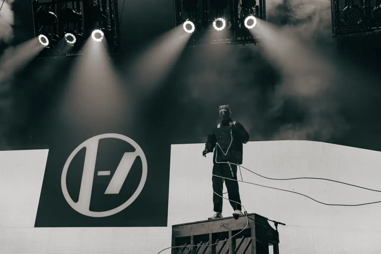 Tyler Joseph z Twenty One Pilots na scenie w Łodzi, w charakterystycznym stroju, na tle logo zespołu.