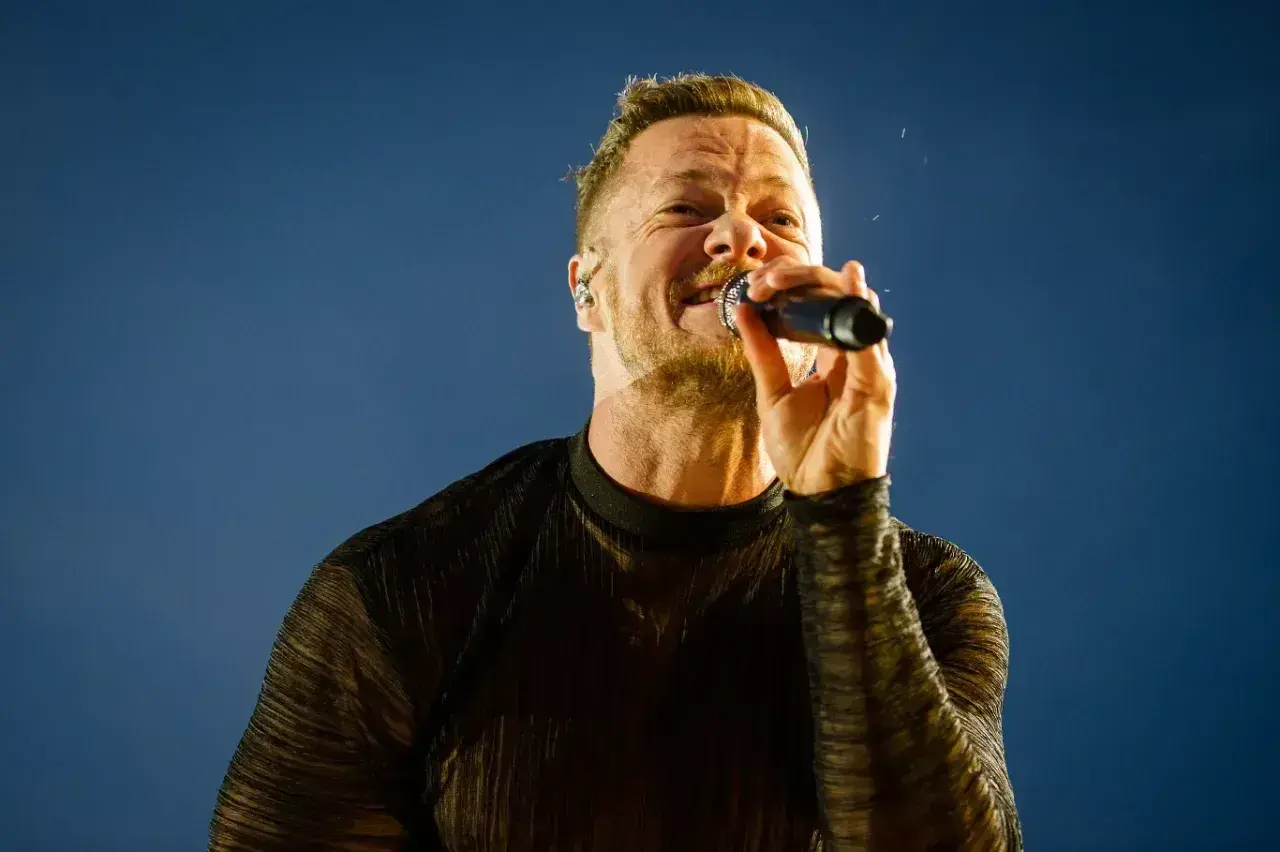 Wokalista Imagine Dragons na koncercie, z mikrofonem w dłoni, śpiewa z pasją.