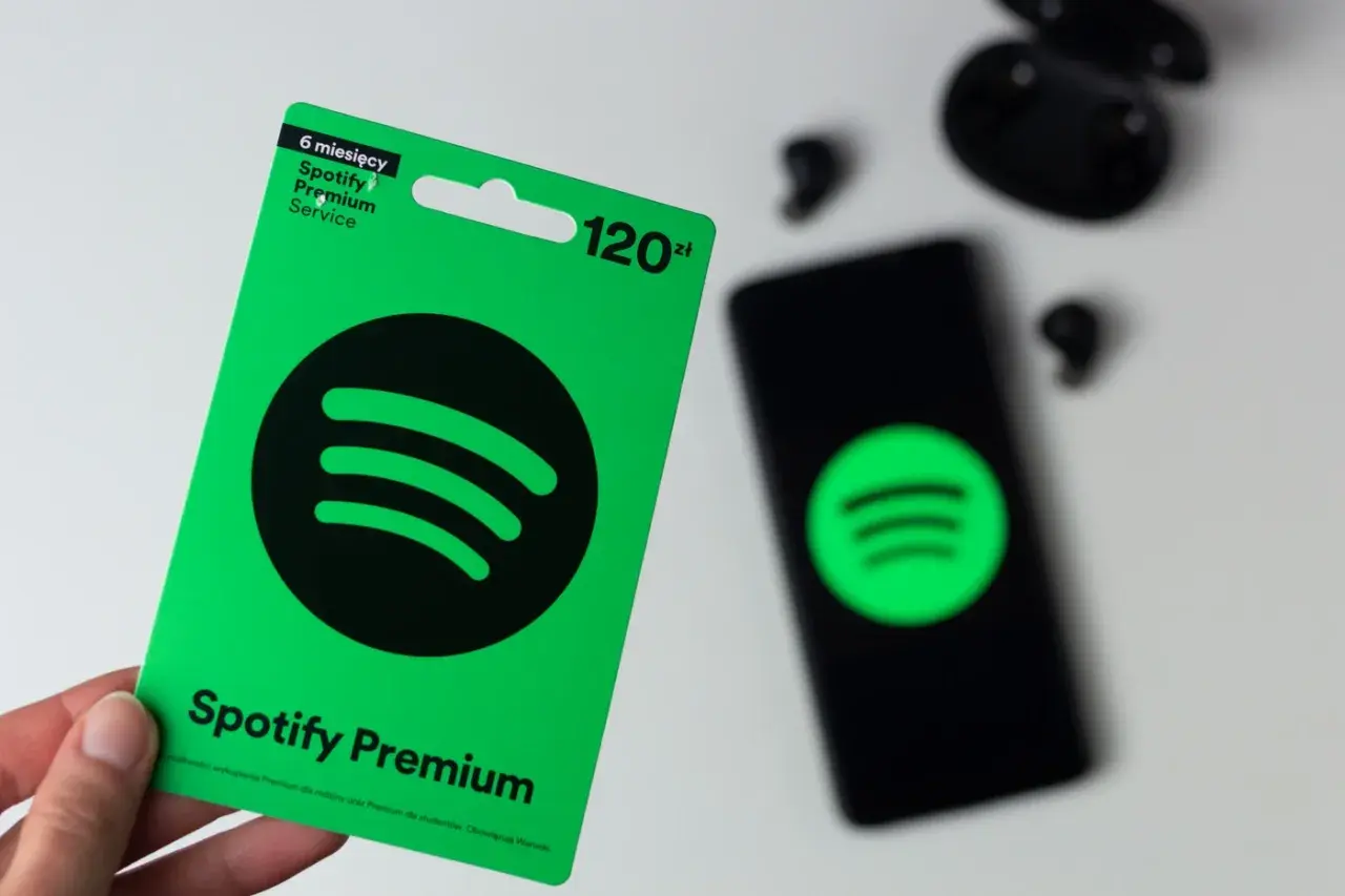 Karta podarunkowa Spotify Premium na 6 miesięcy kosztuje 120 zł. Obok leży smartfon z logo Spotify i słuchawki.