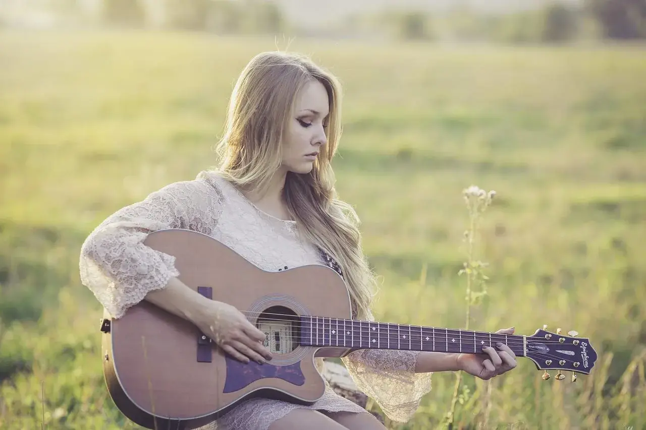 Piękny remaster: młoda kobieta z długimi blond włosami gra na gitarze akustycznej w słonecznym polu.
