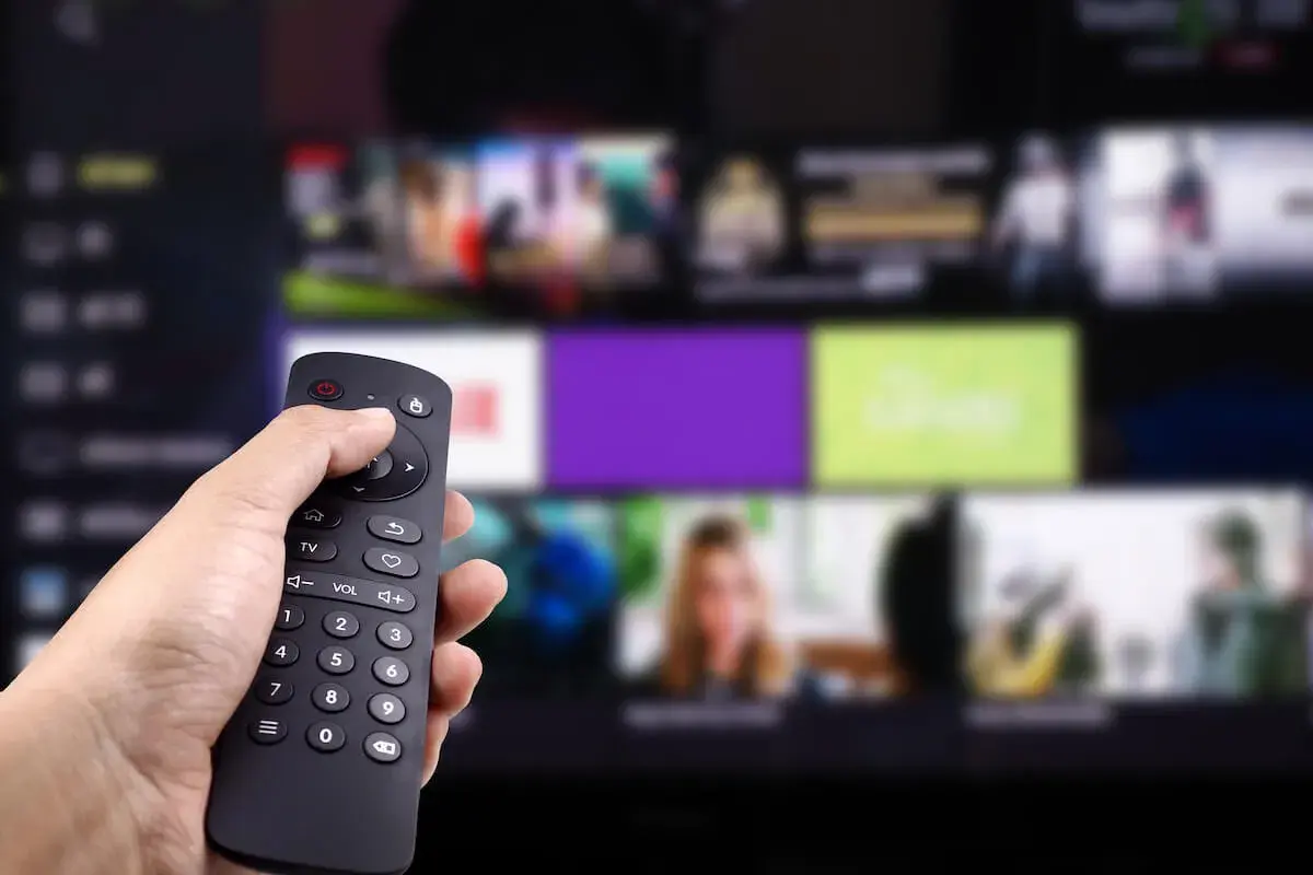 Dłoń trzyma pilot, wybierając program. Zastanawiasz się, kto jest zwolniony z abonamentu RTV? Może Ty?