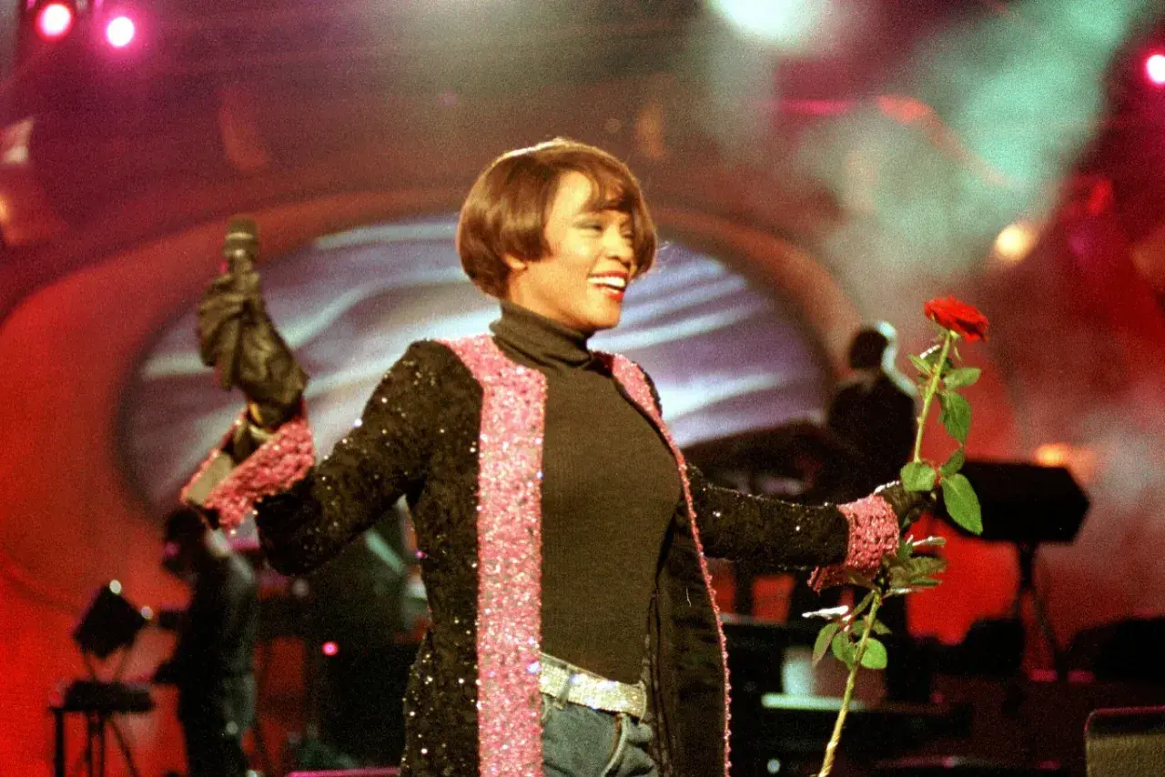 Whitney Houston w Polsce, na scenie z mikrofonem i czerwoną różą, w błyszczącej marynarce.