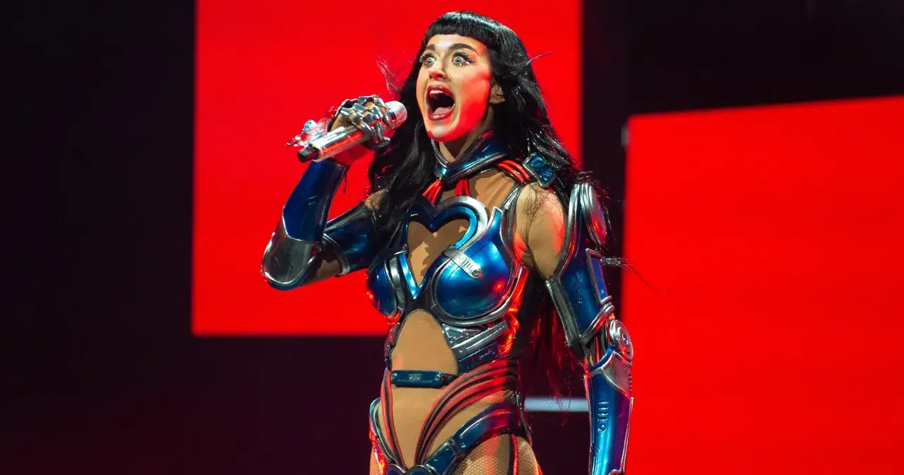 Katy Perry w błyszczącym, niebiesko-srebrnym kostiumie z sercem na piersi śpiewa na scenie w Krakowie.