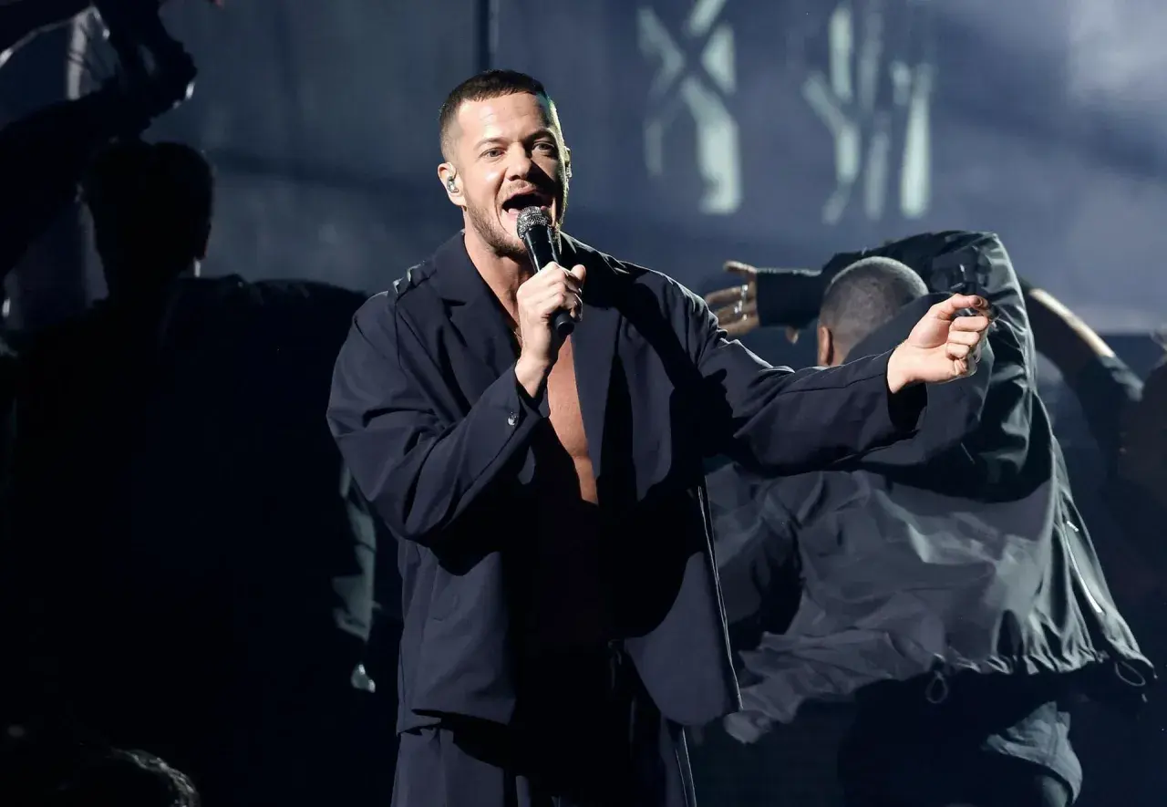 Imagine Dragons koncert Polska: wokalista Dan Reynolds śpiewa na scenie, otoczony tancerzami w mrocznej atmosferze.