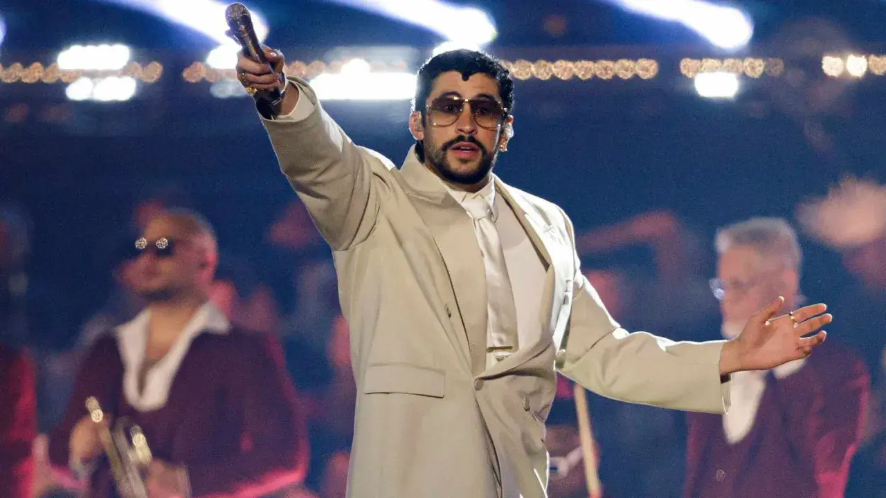 Bad Bunny koncert: artysta w beżowym garniturze z mikrofonem w dłoni, na scenie z tłumem w tle.