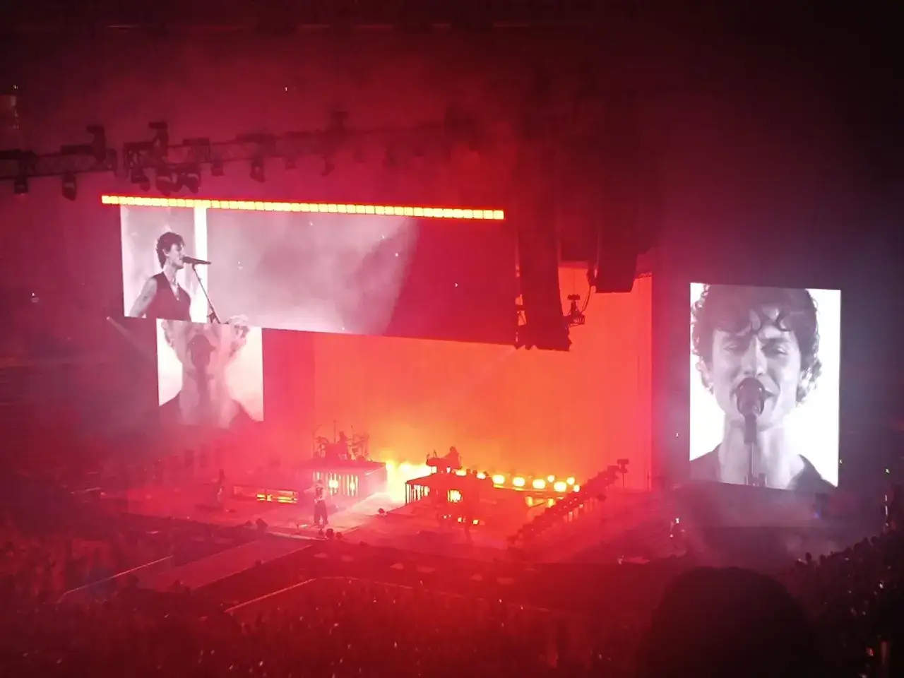 Shawn Mendes koncert w czerwonych światłach. Na ekranach widać zbliżenia artysty, a na scenie gra zespół.