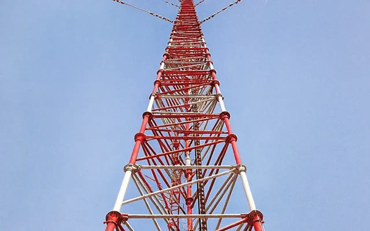 Wysoki, kratownicowy maszt radiowy w Konstantynowie, pomalowany na czerwono-biało, wznosi się ku błękitnemu niebu.