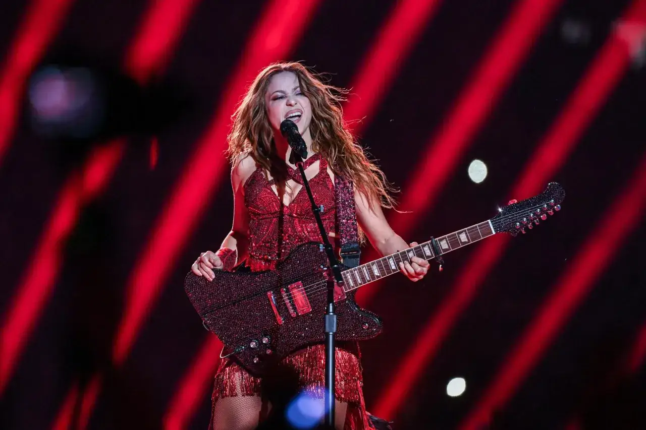Shakira w czerwonym stroju z gitarą na koncercie w Polsce, śpiewa z pasją.