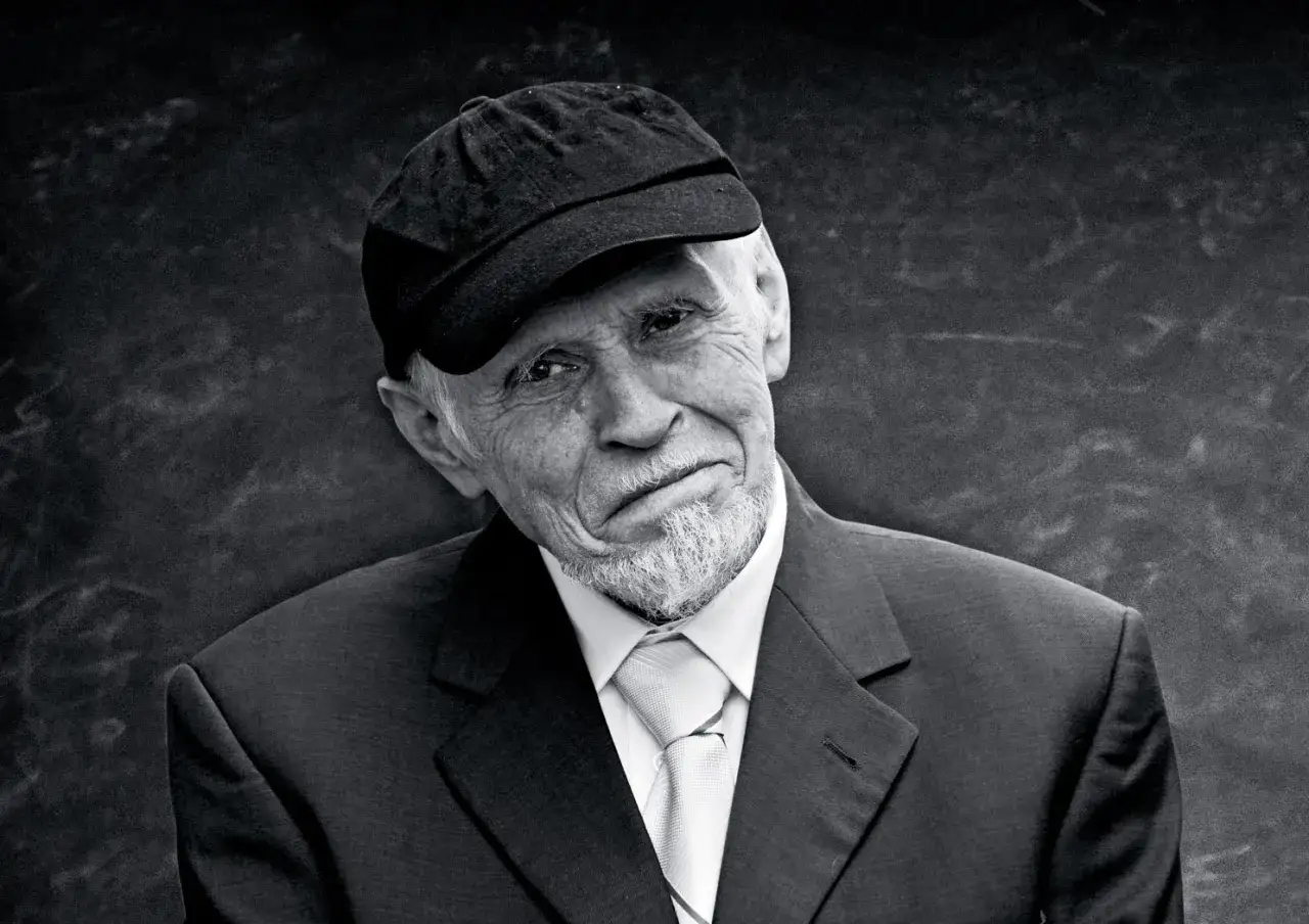 Portret starszego mężczyzny w czapce i garniturze, z charakterystyczną brodą. To Jan Ptaszyn Wróblewski, legendarny muzyk jazzowy.