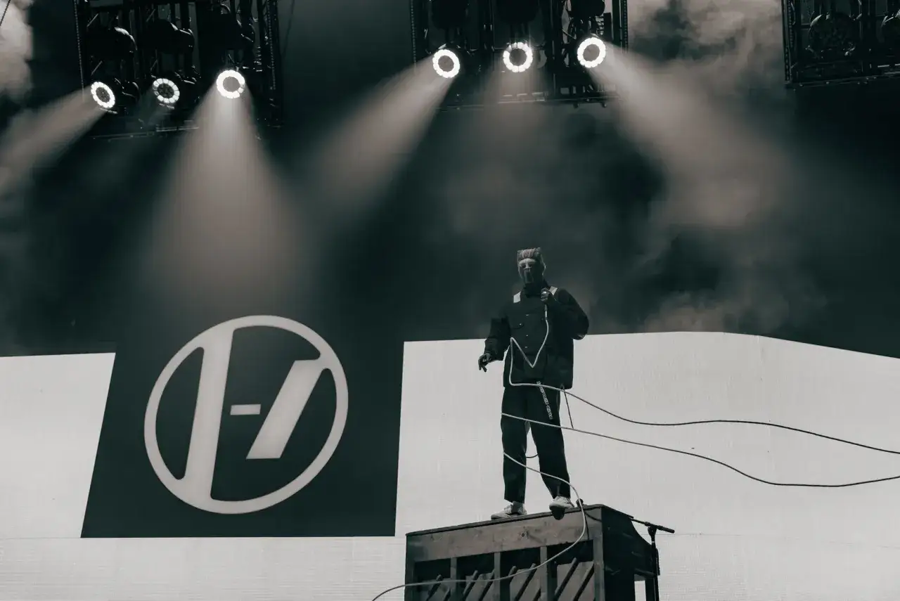 Tyler Joseph z Twenty One Pilots na scenie w Łodzi, w charakterystycznym stroju, na tle logo zespołu.