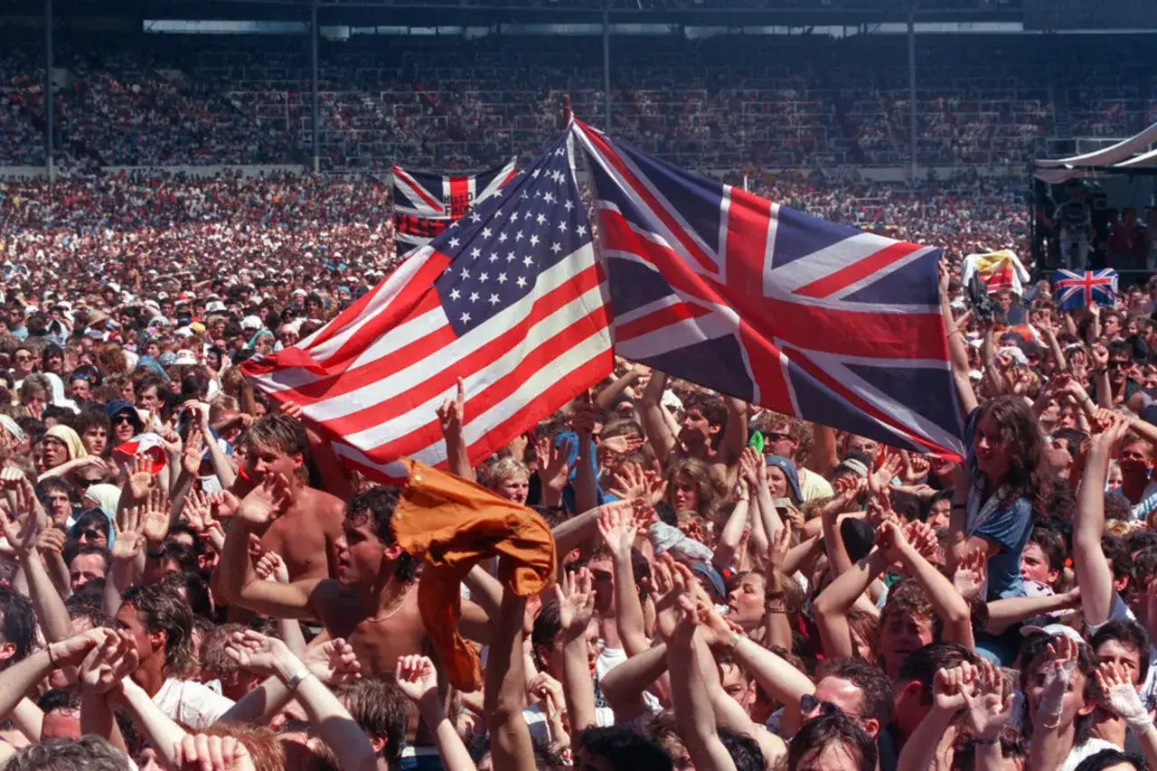 Tłum na koncercie Live Aid unosi flagi USA i Wielkiej Brytanii.