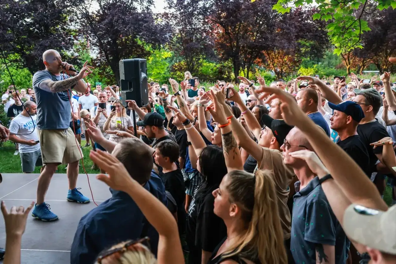 Peja na koncercie, tłum reaguje na jego utwory. Wokalista z mikrofonem, fani z rękami w górze.